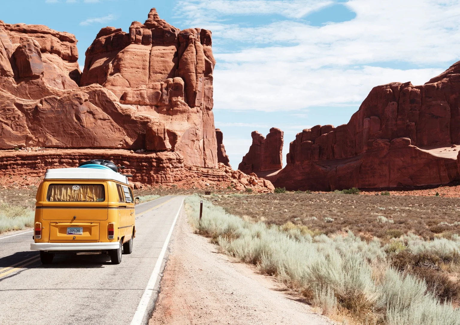 Van jaune sur la route au milieu des canyons rouges, road-trip ouvert
