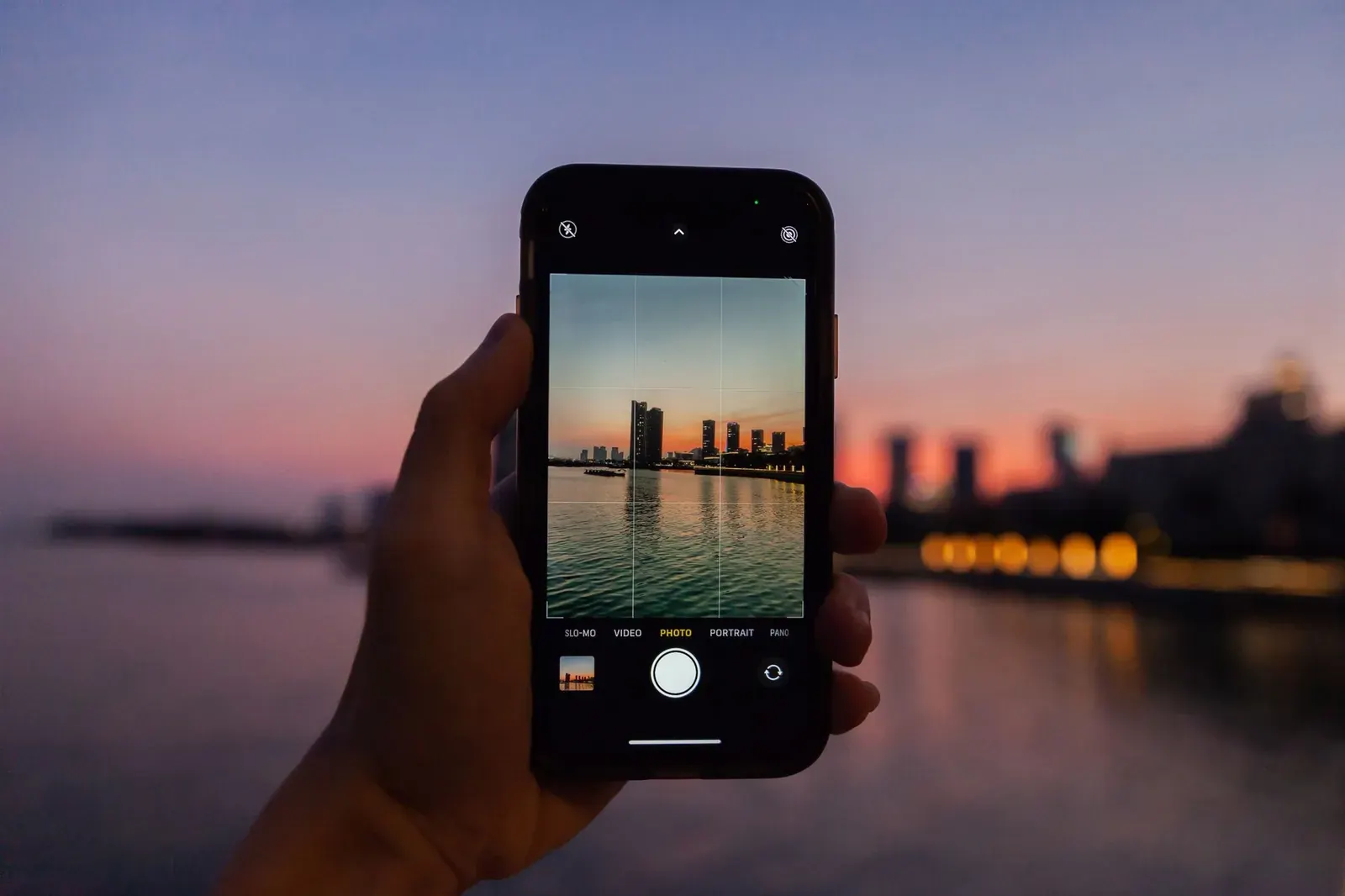 Main tenant un smartphone connecté qui cadre une skyline au crépuscule